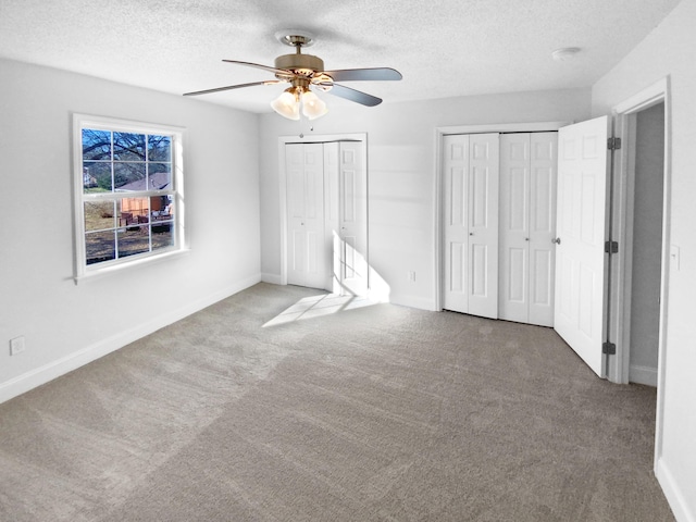 unfurnished bedroom with ceiling fan, carpet, a textured ceiling, and two closets