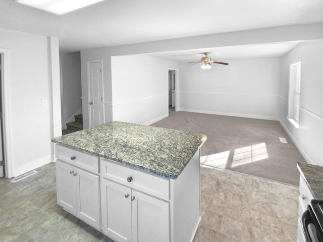 kitchen featuring white cabinetry, dark stone countertops, light carpet, and a kitchen island