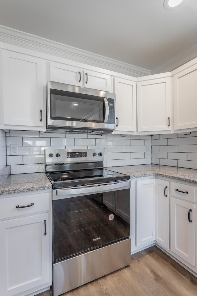 kitchen with tasteful backsplash, white cabinets, stainless steel appliances, and light hardwood / wood-style floors