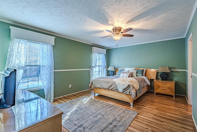 bedroom with a textured ceiling, light hardwood / wood-style flooring, ornamental molding, and ceiling fan