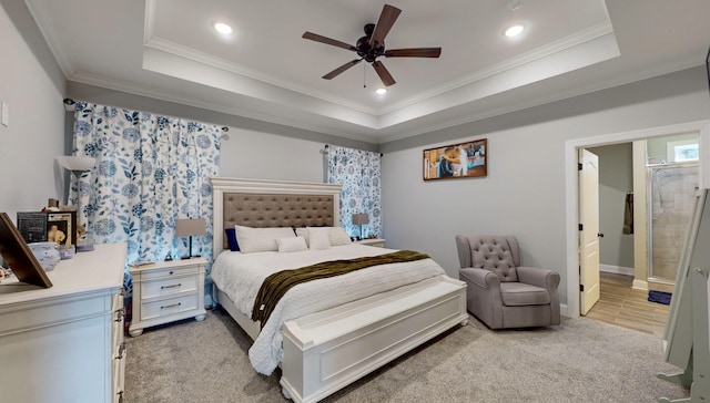 carpeted bedroom featuring a tray ceiling, ensuite bathroom, ornamental molding, and ceiling fan