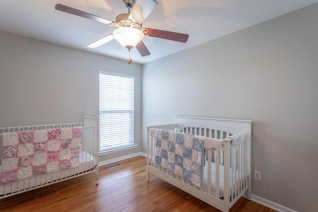 bedroom featuring ceiling fan, multiple windows, hardwood / wood-style floors, and a crib