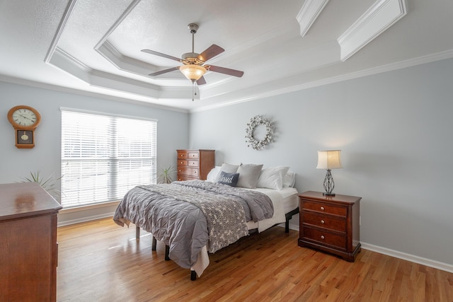 bedroom with ceiling fan, a tray ceiling, crown molding, and light wood-type flooring