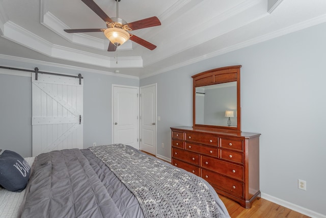 bedroom with a raised ceiling, ceiling fan, light hardwood / wood-style flooring, crown molding, and a barn door