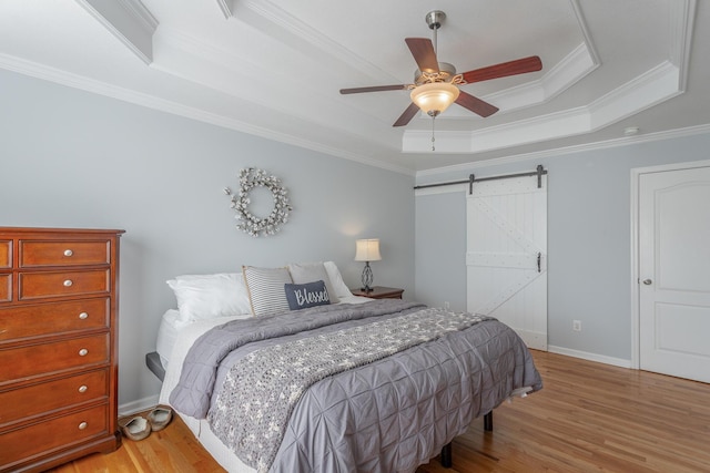 bedroom featuring ceiling fan, a barn door, a raised ceiling, crown molding, and light wood-type flooring