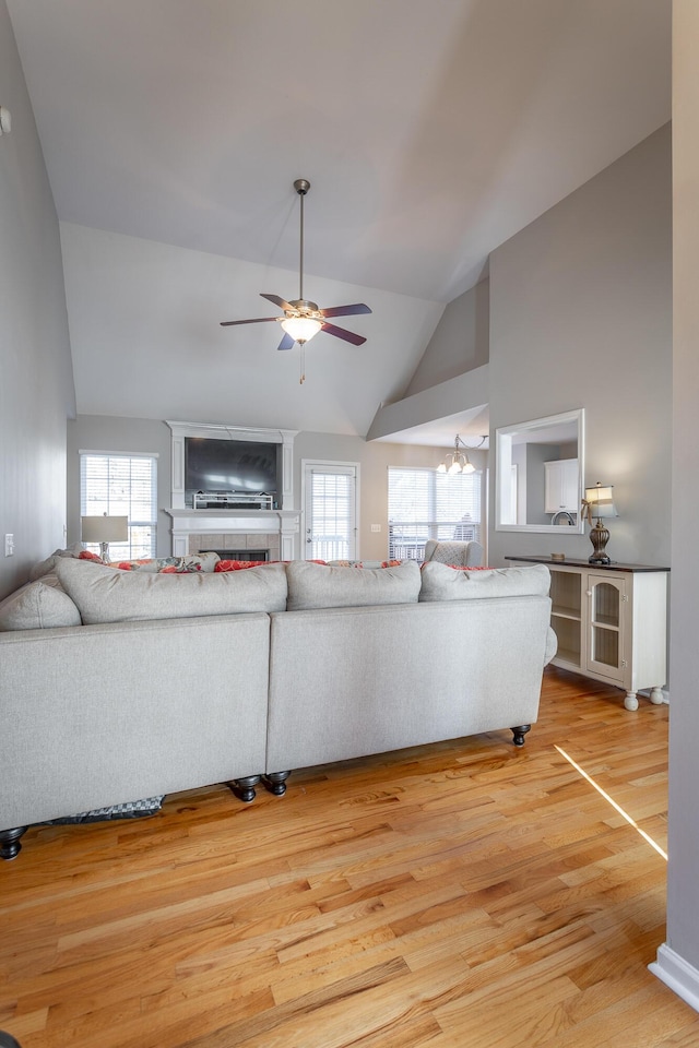 living room featuring vaulted ceiling, a fireplace, ceiling fan with notable chandelier, and hardwood / wood-style flooring