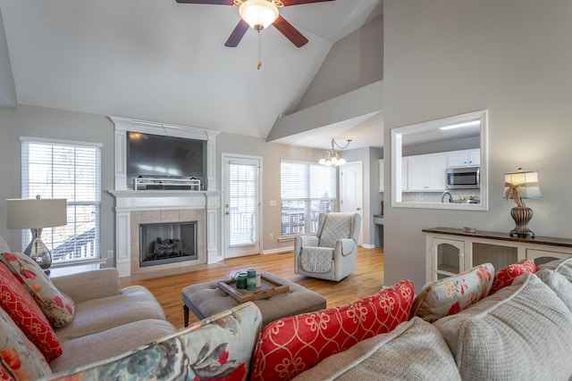 living room featuring vaulted ceiling, a fireplace, ceiling fan with notable chandelier, and light hardwood / wood-style flooring