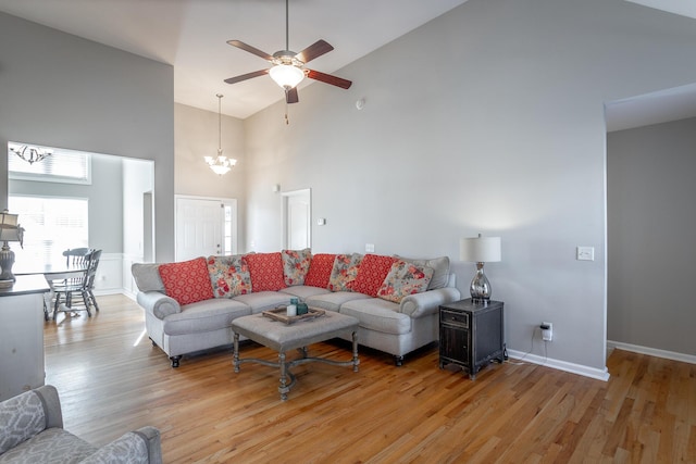 living room featuring ceiling fan with notable chandelier, light hardwood / wood-style flooring, and high vaulted ceiling