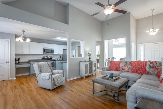 living room with ceiling fan with notable chandelier, a high ceiling, and light hardwood / wood-style flooring