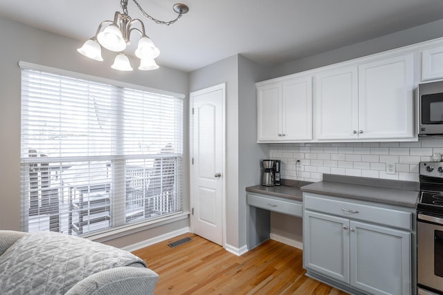 kitchen featuring backsplash, pendant lighting, white cabinetry, light hardwood / wood-style flooring, and stainless steel appliances