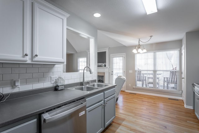 kitchen with tasteful backsplash, light wood-type flooring, vaulted ceiling, stainless steel dishwasher, and sink