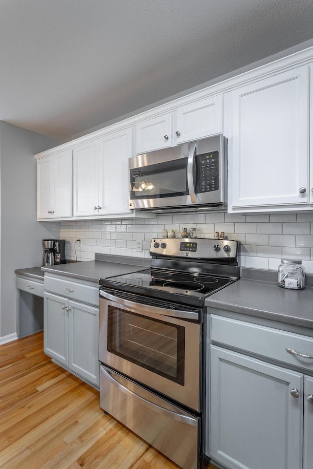 kitchen featuring backsplash, white cabinetry, appliances with stainless steel finishes, and light hardwood / wood-style flooring