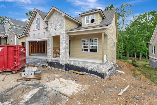 view of front of property featuring covered porch, cooling unit, a shingled roof, and an attached garage