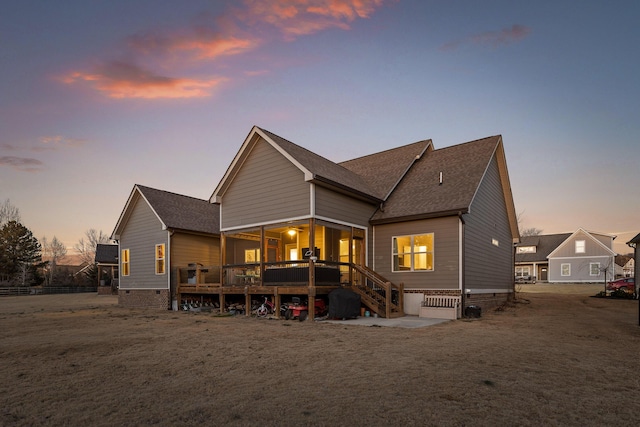 back house at dusk featuring a wooden deck and a yard