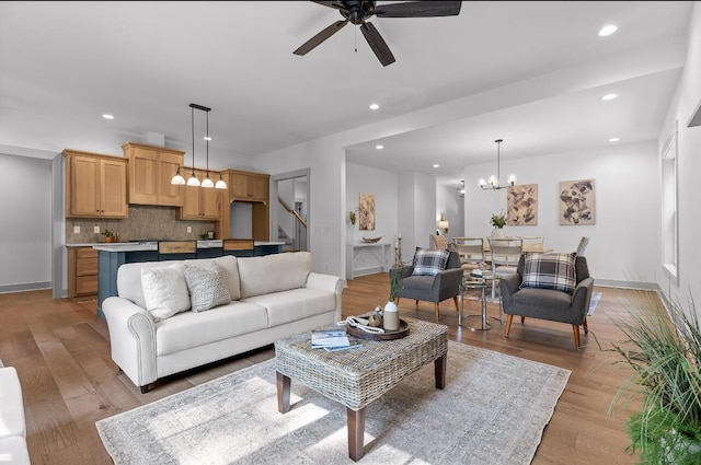 living room with ceiling fan with notable chandelier and light hardwood / wood-style floors