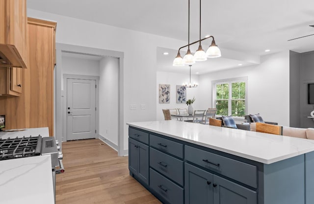 kitchen with decorative light fixtures, a center island, light hardwood / wood-style floors, stainless steel range with gas stovetop, and light stone countertops