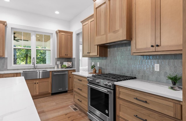 kitchen with stainless steel appliances, tasteful backsplash, light stone countertops, light hardwood / wood-style flooring, and sink