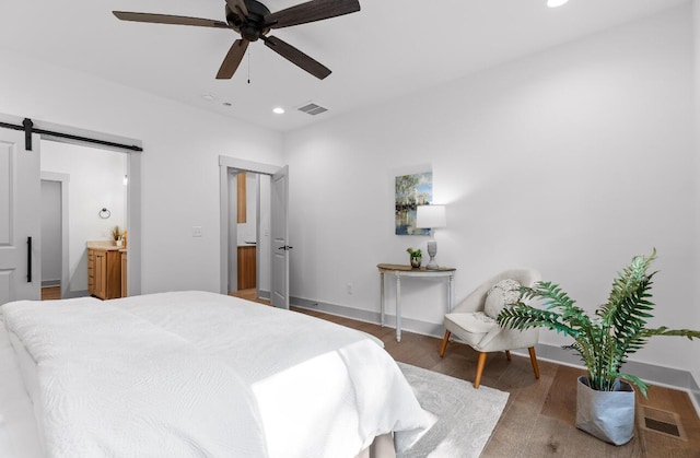 bedroom featuring ceiling fan, a barn door, and dark wood-type flooring