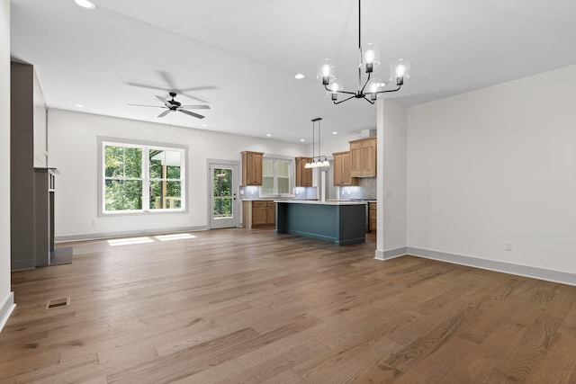 unfurnished living room featuring light wood-type flooring and ceiling fan with notable chandelier