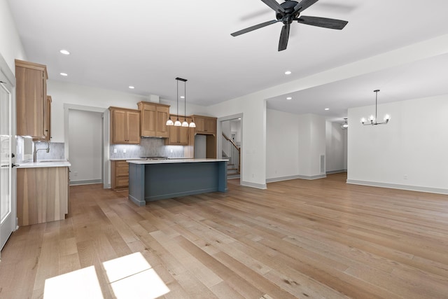 kitchen with backsplash, a spacious island, light hardwood / wood-style floors, pendant lighting, and ceiling fan with notable chandelier