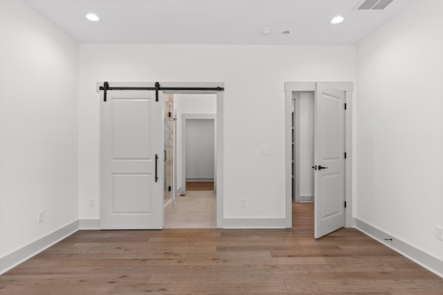 unfurnished bedroom with a barn door and light hardwood / wood-style flooring