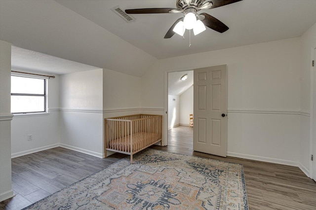 unfurnished bedroom featuring ceiling fan, lofted ceiling, a crib, and hardwood / wood-style flooring