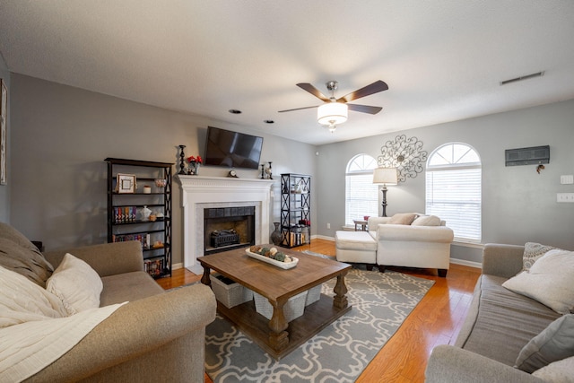 living room featuring a tiled fireplace, light wood-type flooring, and ceiling fan