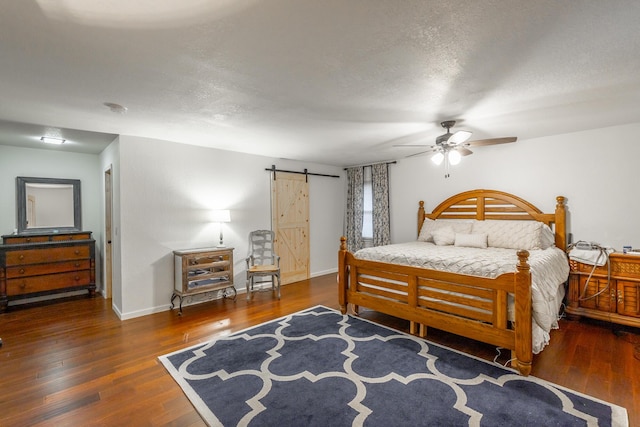 bedroom with ceiling fan, dark hardwood / wood-style floors, a barn door, and a textured ceiling