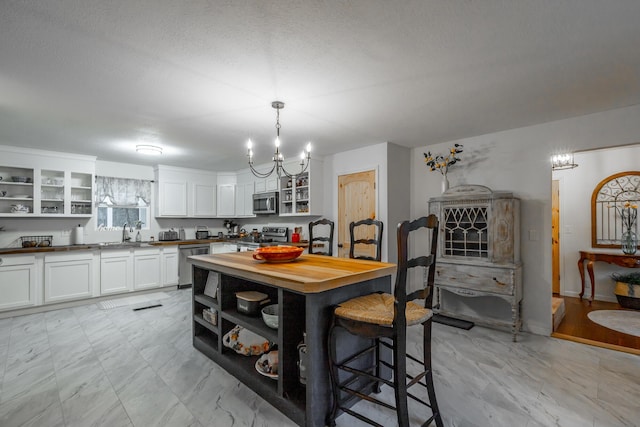 kitchen with sink, butcher block countertops, hanging light fixtures, appliances with stainless steel finishes, and white cabinets