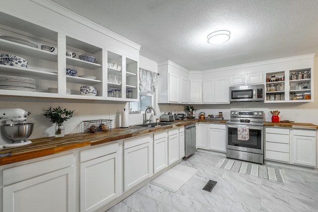 kitchen with butcher block countertops, sink, stainless steel appliances, a textured ceiling, and white cabinets