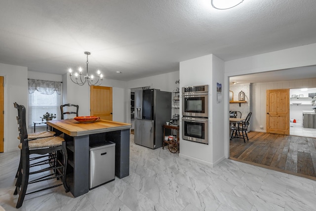 kitchen with appliances with stainless steel finishes, a textured ceiling, a kitchen bar, decorative light fixtures, and a chandelier