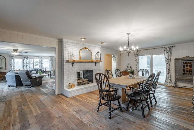 dining room featuring a fireplace, crown molding, wood-type flooring, and ceiling fan with notable chandelier