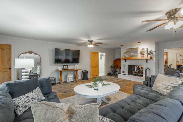 living room featuring a brick fireplace, ceiling fan, and light wood-type flooring