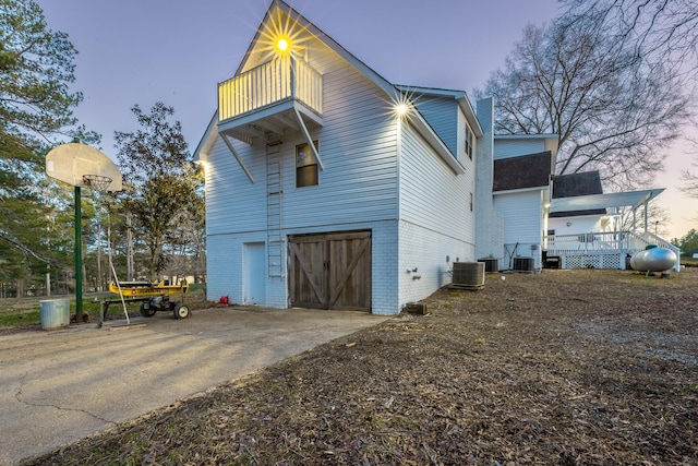 property exterior at dusk featuring central AC, a balcony, and a garage