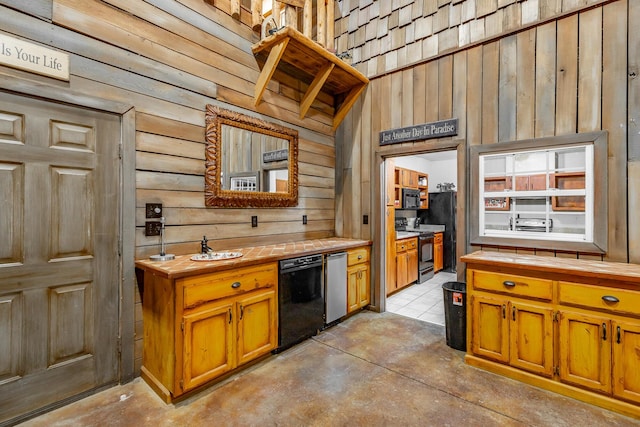 kitchen with tile countertops, wooden walls, and black appliances