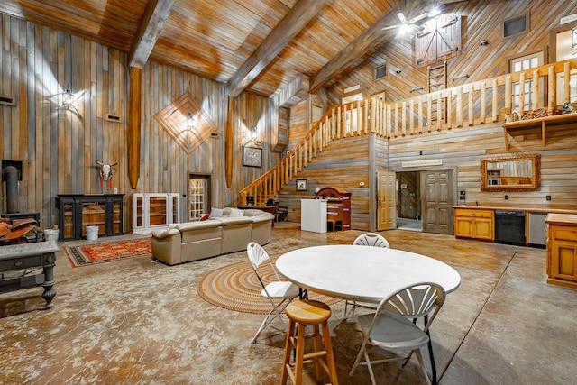 dining space featuring beamed ceiling, a wood stove, wooden walls, and a towering ceiling