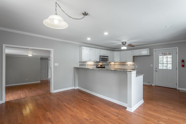 kitchen featuring white cabinetry, hanging light fixtures, kitchen peninsula, light stone counters, and crown molding