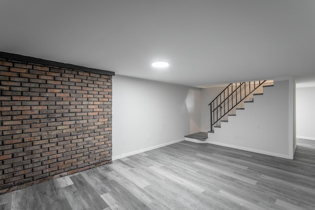 basement featuring wood-type flooring and brick wall