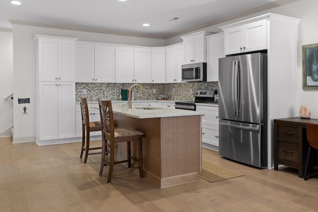 kitchen with white cabinetry, sink, a kitchen bar, stainless steel appliances, and a center island with sink