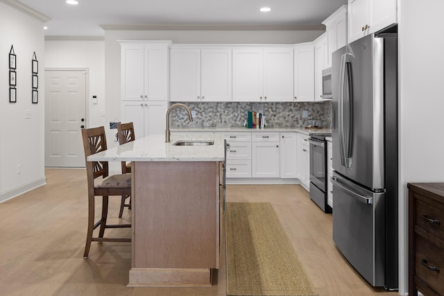 kitchen with a breakfast bar area, white cabinetry, an island with sink, stainless steel appliances, and light stone countertops