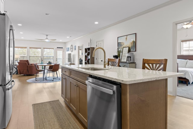 kitchen with an island with sink, sink, ceiling fan, stainless steel appliances, and light stone countertops