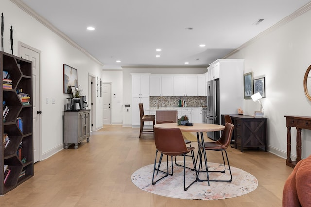 dining space with crown molding, sink, and light hardwood / wood-style flooring