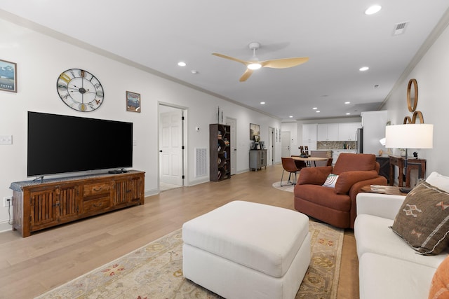 living room featuring ceiling fan, ornamental molding, and light wood-type flooring