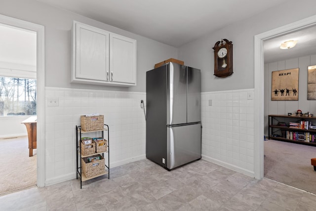 kitchen featuring light carpet, tile walls, stainless steel refrigerator, and white cabinets