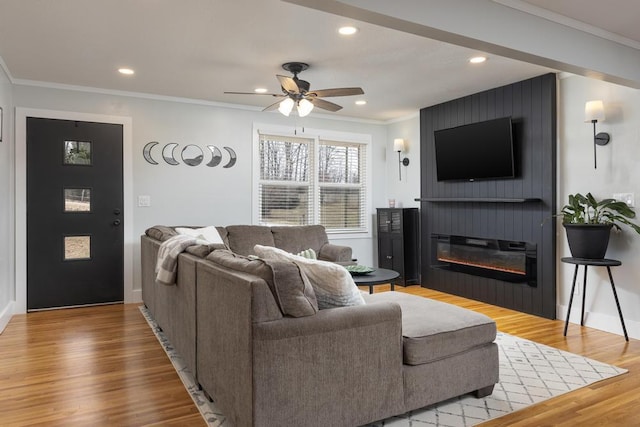 living room featuring crown molding, hardwood / wood-style floors, ceiling fan, and a large fireplace