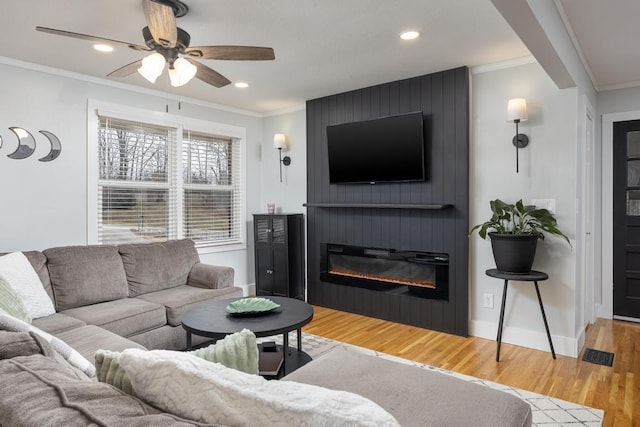 living room with crown molding, hardwood / wood-style floors, ceiling fan, and a large fireplace