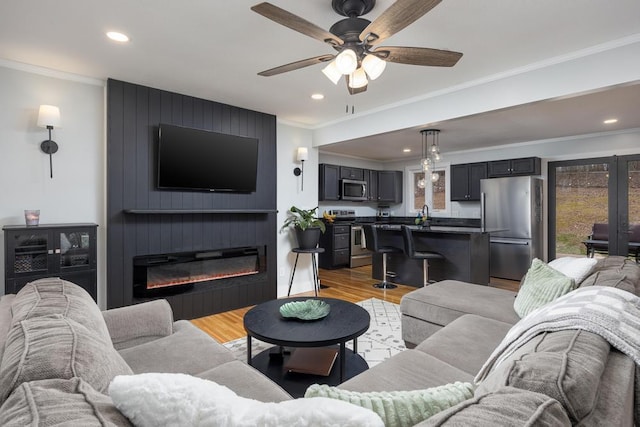 living room featuring crown molding, light wood-type flooring, ceiling fan, and a large fireplace