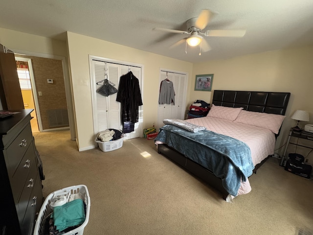 bedroom featuring multiple closets, ceiling fan, a textured ceiling, and light carpet