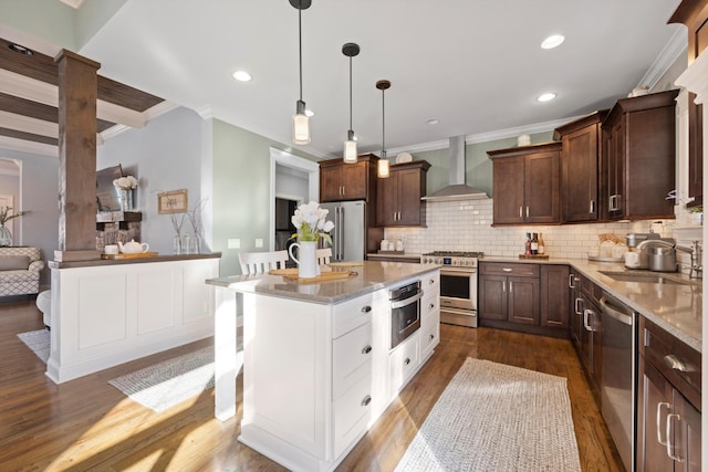 kitchen featuring sink, premium appliances, decorative backsplash, hanging light fixtures, and wall chimney range hood