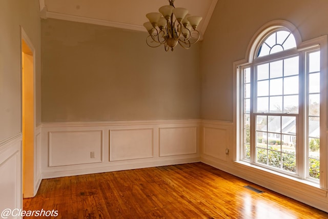 empty room featuring hardwood / wood-style flooring, ornamental molding, lofted ceiling, and a notable chandelier